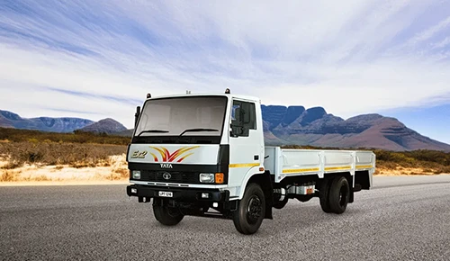 White Tata LPT 1216 dropside flatbed truck parked on an open road with a Mountain in the background