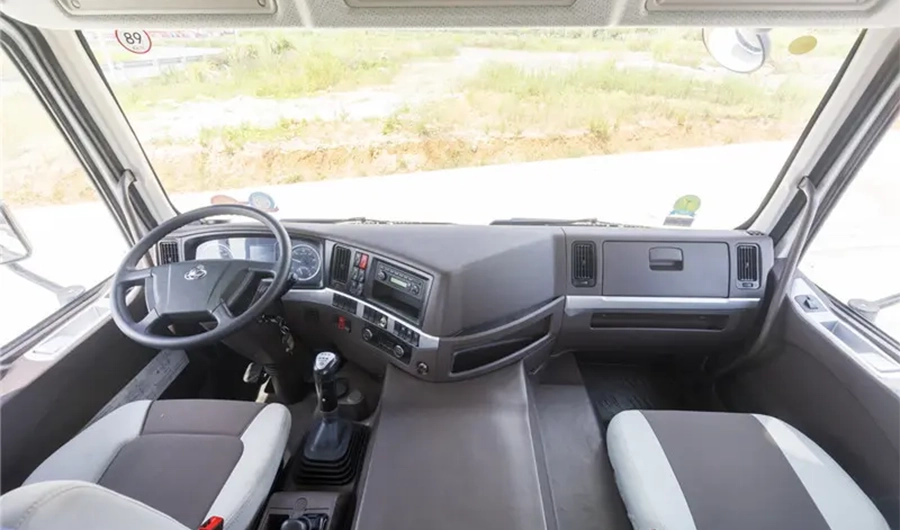 Chenglong heavy-duty truck cab interior showing driver and passenger seats, steering wheel, manual gear lever and dashboard controls