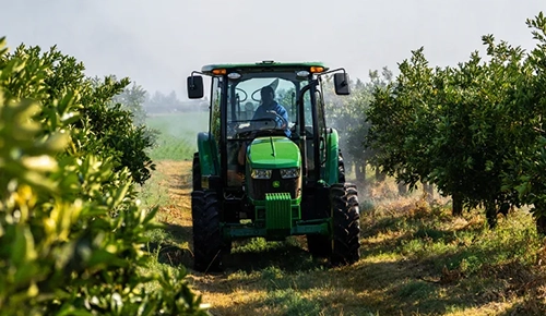 A John Deere 5EN Series narrow cab tractor driving down an orchard row.