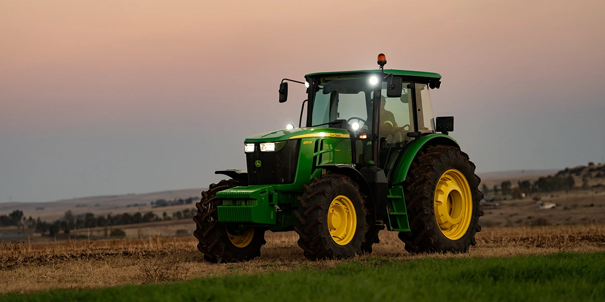 John Deere 6B Series tractor parked in an agricultural field at dusk