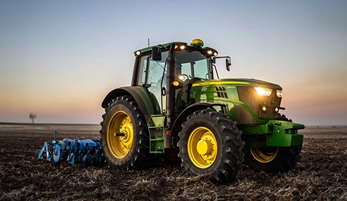John Deere 6M Series agricultural tractor tilling field at dusk