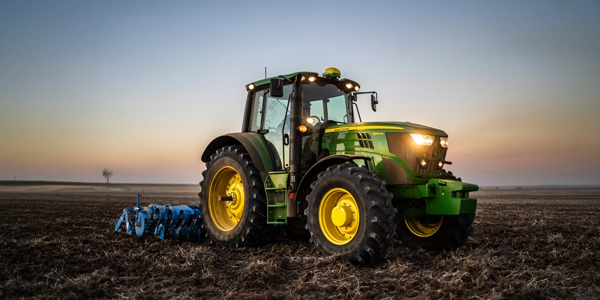 John Deere 6M Series agricultural tractor tilling field at dusk