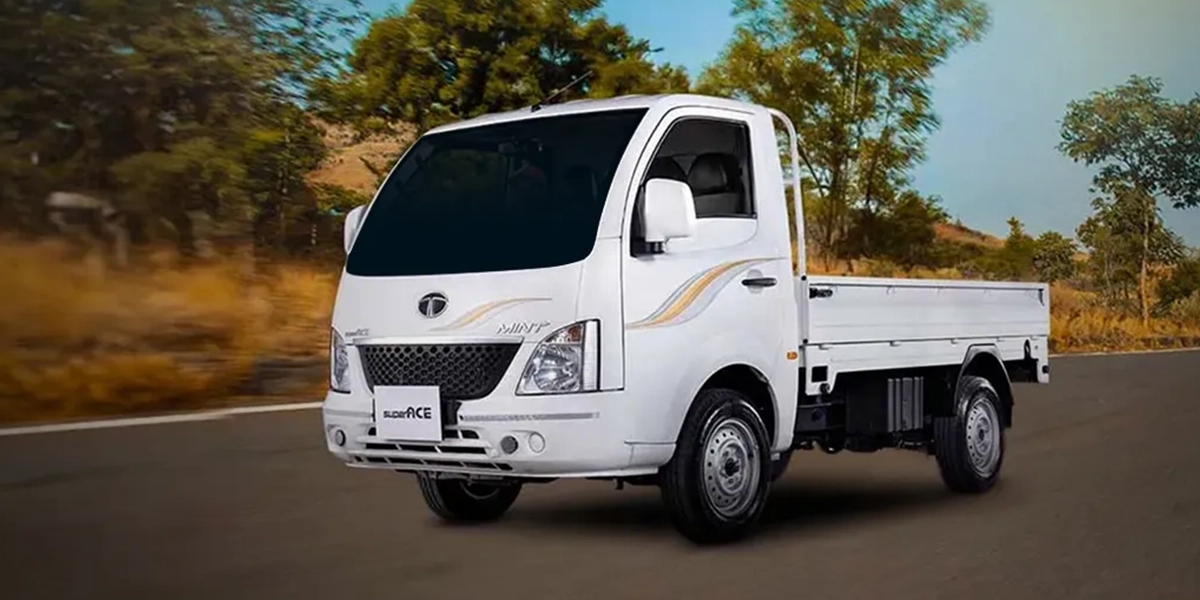 White Tata Super Ace mini truck driving on a paved road with trees and hills in the background.