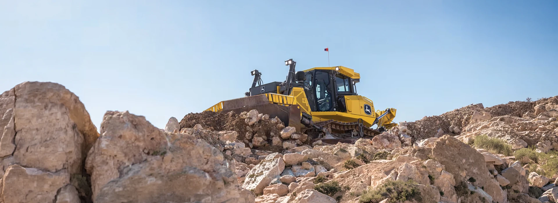 John Deere crawler dozer pushing rocks and earth on a steep rocky terrain