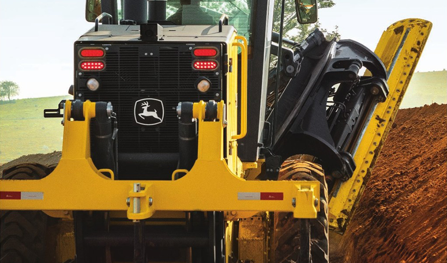 Rear view of John Deere construction machine working through soil with side-mounted earthmoving attachment