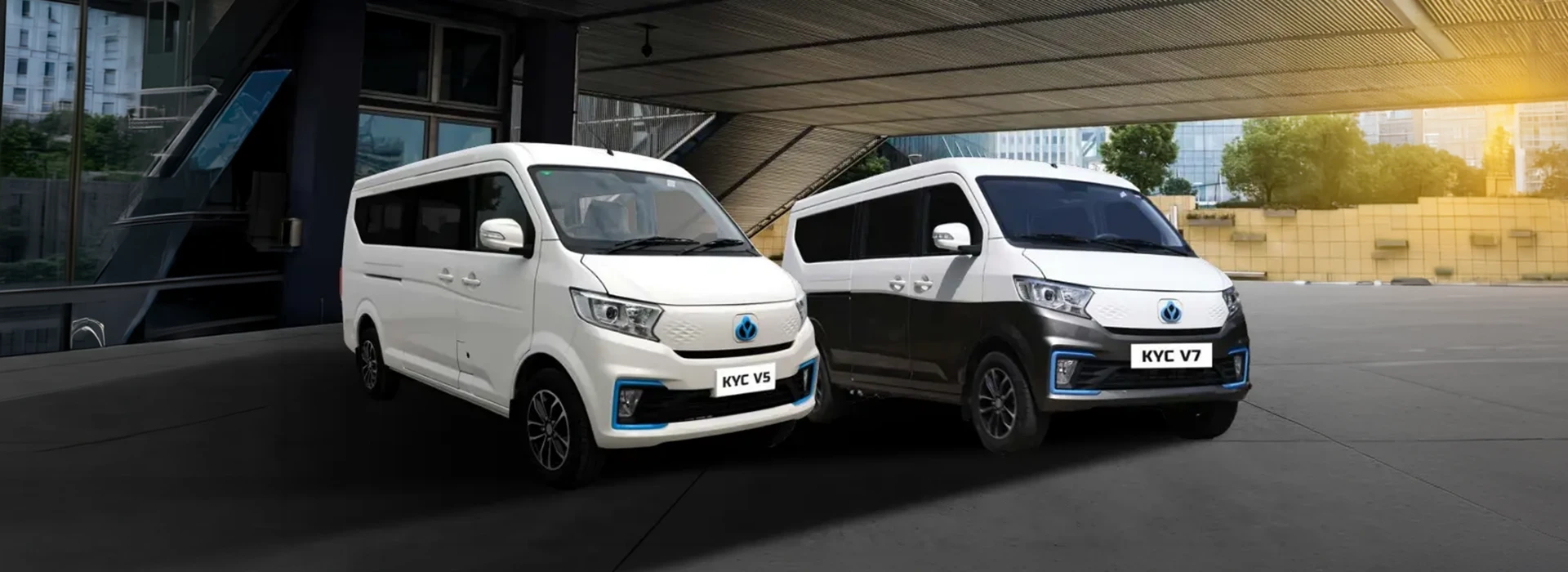 White Tata KYC V5 and two-tone KYC V7 electric vans parked outside a modern commercial building