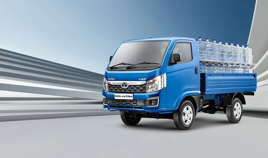 Blue Tata Intra V20 pickup truck loaded with large water bottles on a paved surface.