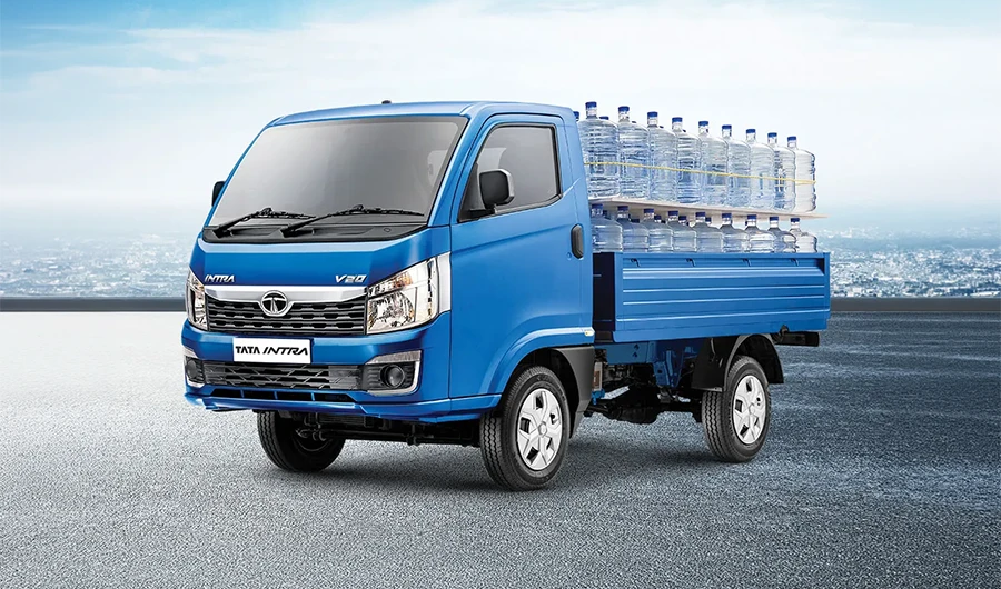 Blue Tata Intra V20 pickup truck loaded with large water bottles on a paved surface.