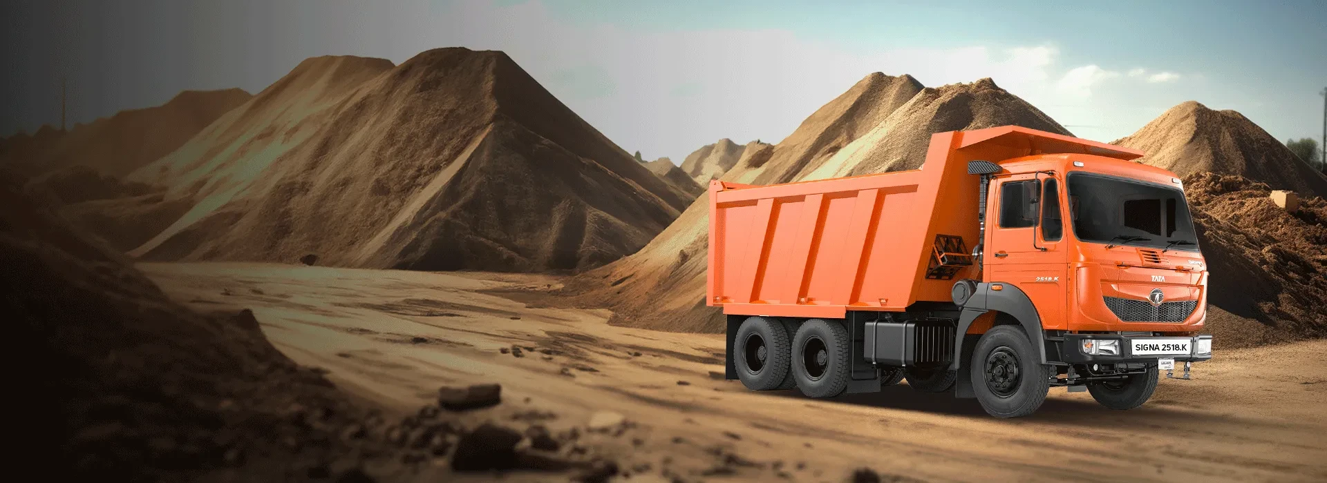 Orange Tata Signa 2518.K tipper truck parked in front of large earth mounds at a construction site.
