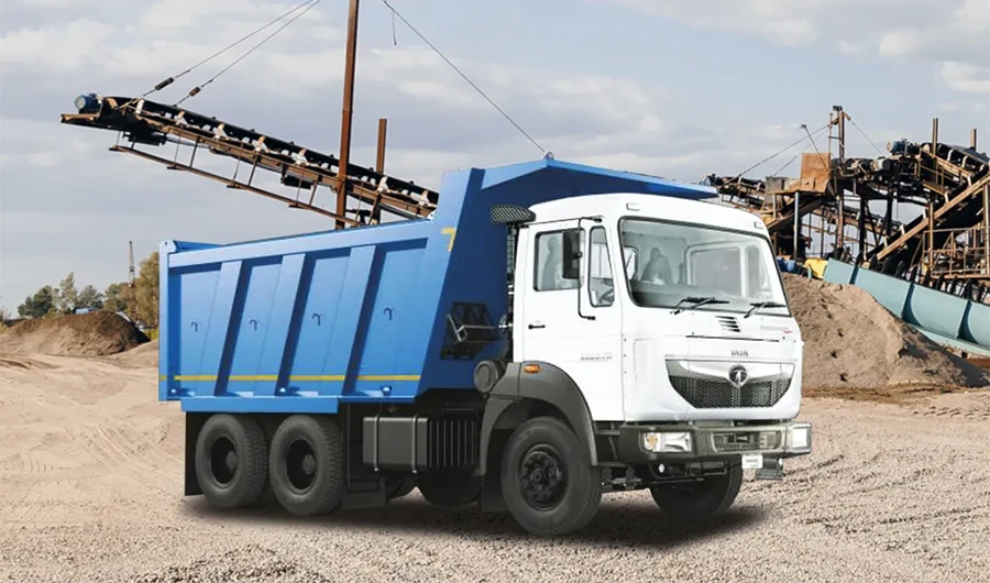 A white and blue Tata Signa heavy-duty tipper truck parked at an industrial quarry or mining site with conveyor belts and gravel piles in the background.