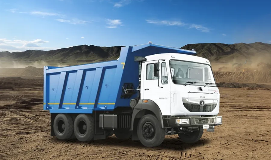 A white and blue Tata Signa heavy-duty tipper truck parked on a dusty construction or mining site with rolling hills in the background.