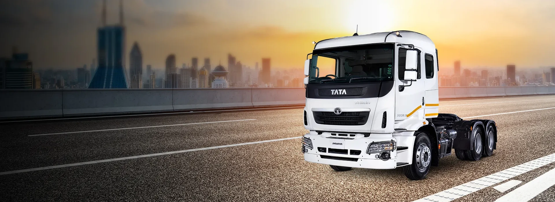 White Tata Prima 5038.S heavy-duty commercial truck parked on a highway with a city skyline in the background at sunset