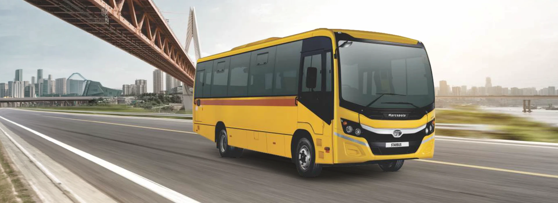 Yellow Tata Starbus Prime Marcopolo bus driving on a highway with a large bridge in the background