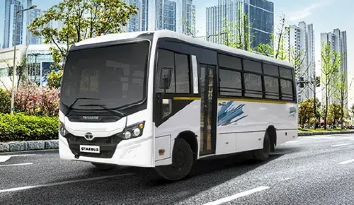 White Tata Starbus Prime passenger bus driving on an urban city street with modern buildings in the background