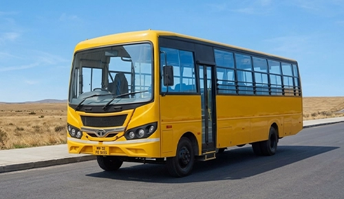 A yellow school bus parked on an asphalt road under a clear blue sky, with open grassy fields in the background.