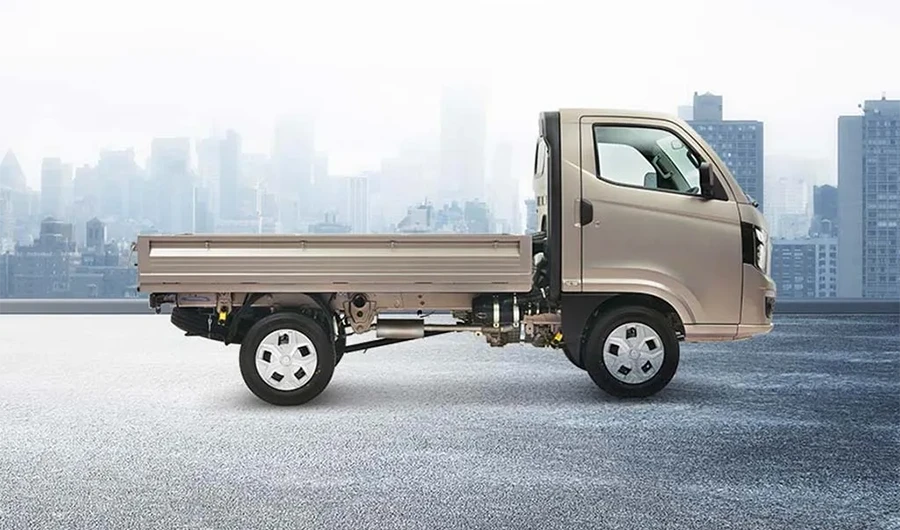 Side profile of a silver Tata Intra V10 mini truck featuring an empty drop-side cargo bed against a city skyline background