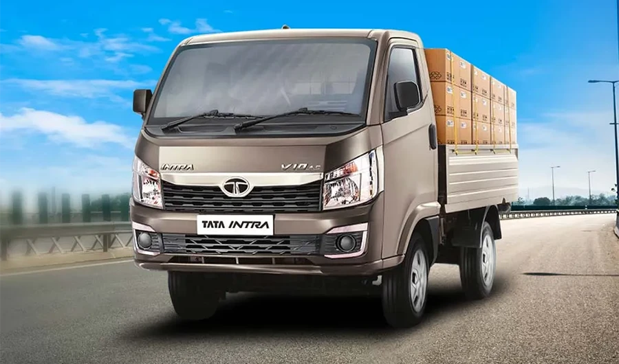 Front three-quarter view of a silver Tata Intra V10 AC mini truck loaded with stacked cargo boxes on an open highwa