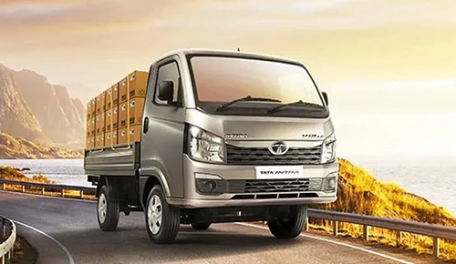 Silver Tata Intra V10 light commercial truck loaded with cargo boxes driving along a scenic coastal road at sunset