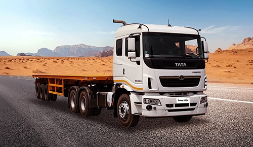 White Tata Prima 6038.S tractor head with yellow flatbed trailer on a desert highway