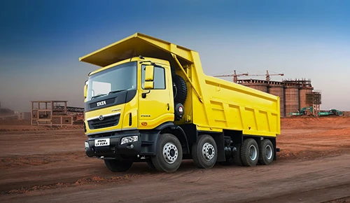 Yellow Tata Prima 3128.K 8x4 tipper truck parked at a construction site with industrial structures