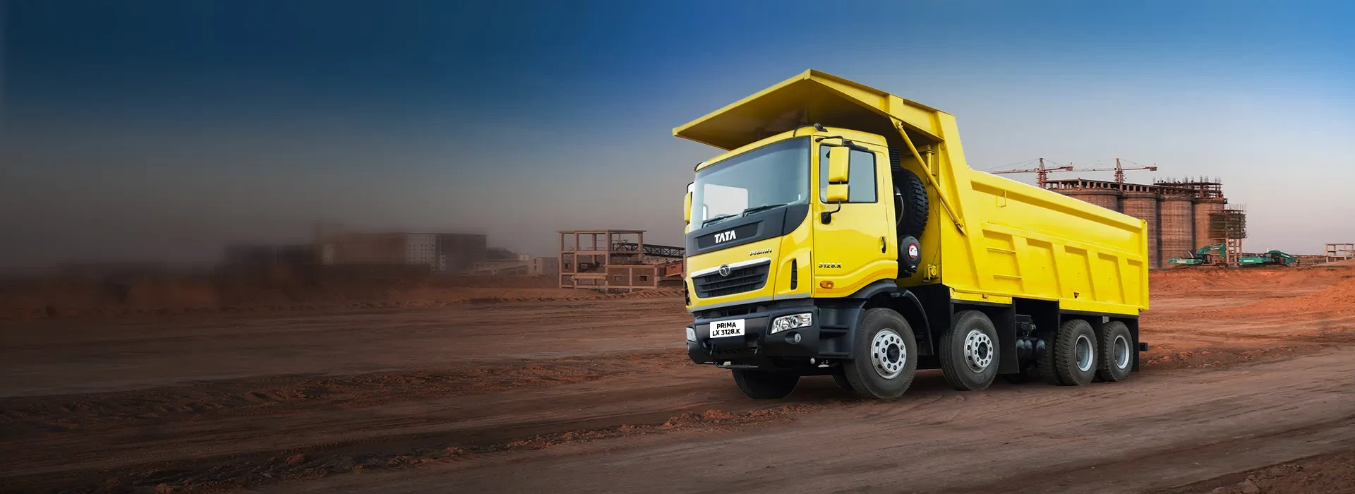 Yellow Tata Prima 3128.K 8x4 tipper truck parked at a construction site with industrial structures