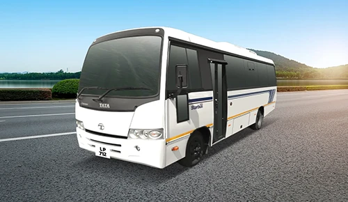 White Tata LP 712 Starbus passenger bus parked on a paved road with tree-lined lake background
