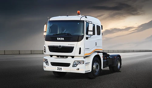 A front three-quarter view of a white Tata Prima 4438.S heavy-duty truck tractor driving on an open asphalt highway under a dramatic, overcast evening sky.
