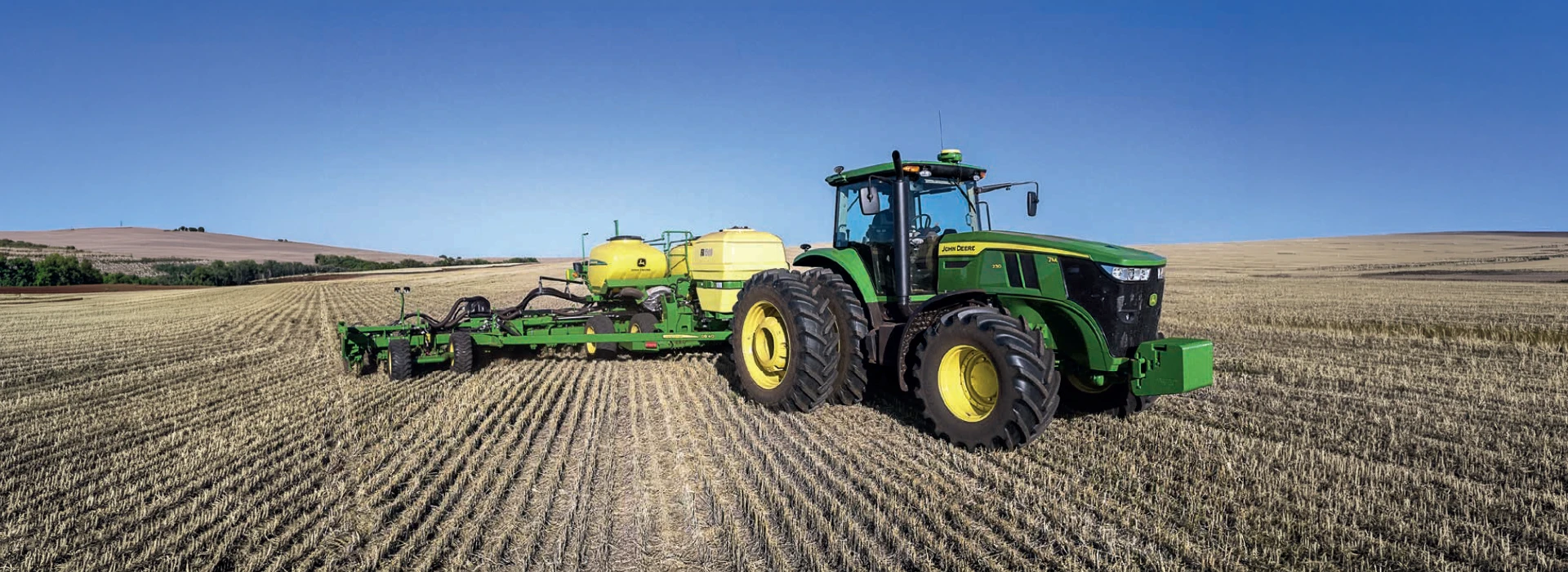 ohn Deere 7M Series tractor pulling a planter in an agricultural field