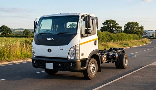 A front three-quarter view of a white Tata Ultra 814 chassis-cab truck driving on a country road at dusk, with fields and trees in the background under a blue sky.