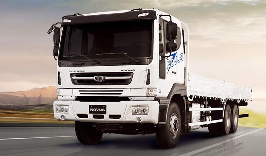 White Daewoo Novus flatbed truck driving along an open highway at sunset