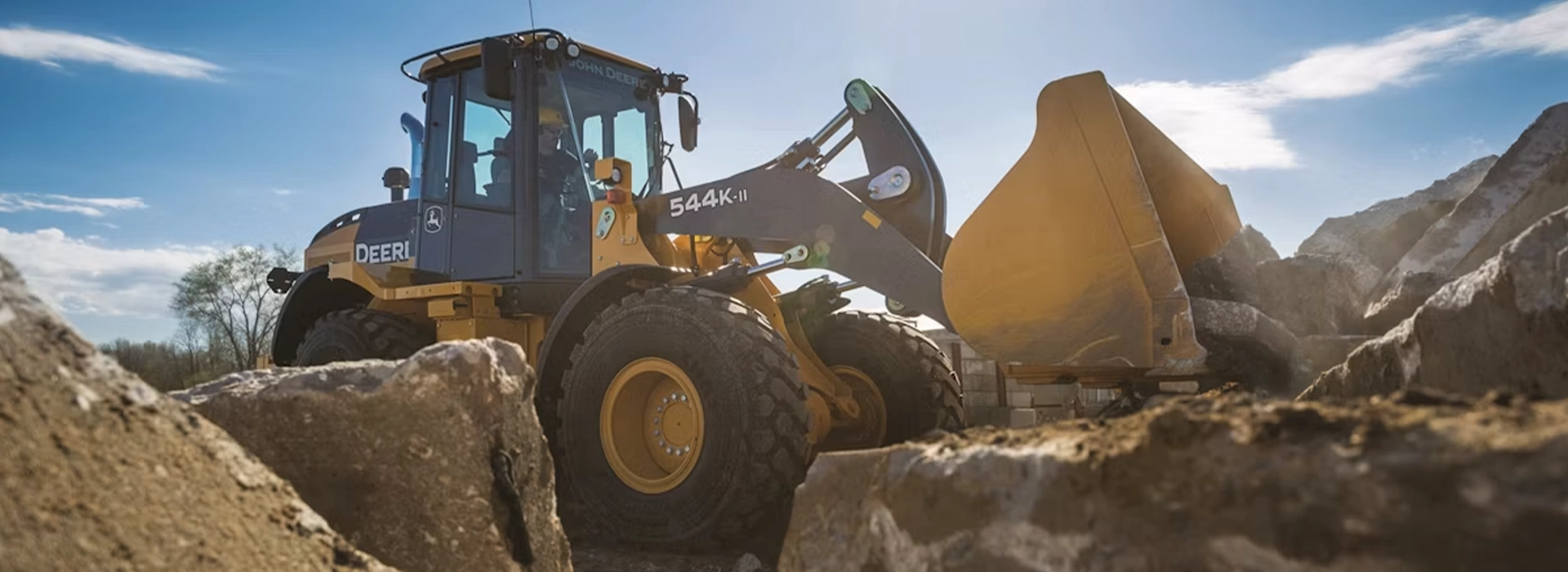 John Deere wheel loader with raised front bucket operating on a rocky construction site