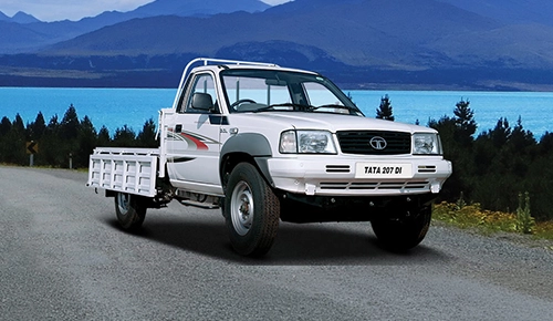 White Tata 207 DI single-cab pickup truck with a drop-side cargo bed parked on a scenic mountain road
