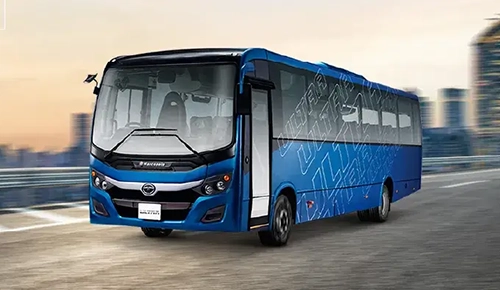 Blue Tata Ultra passenger bus driving on a city highway with tall buildings in the background