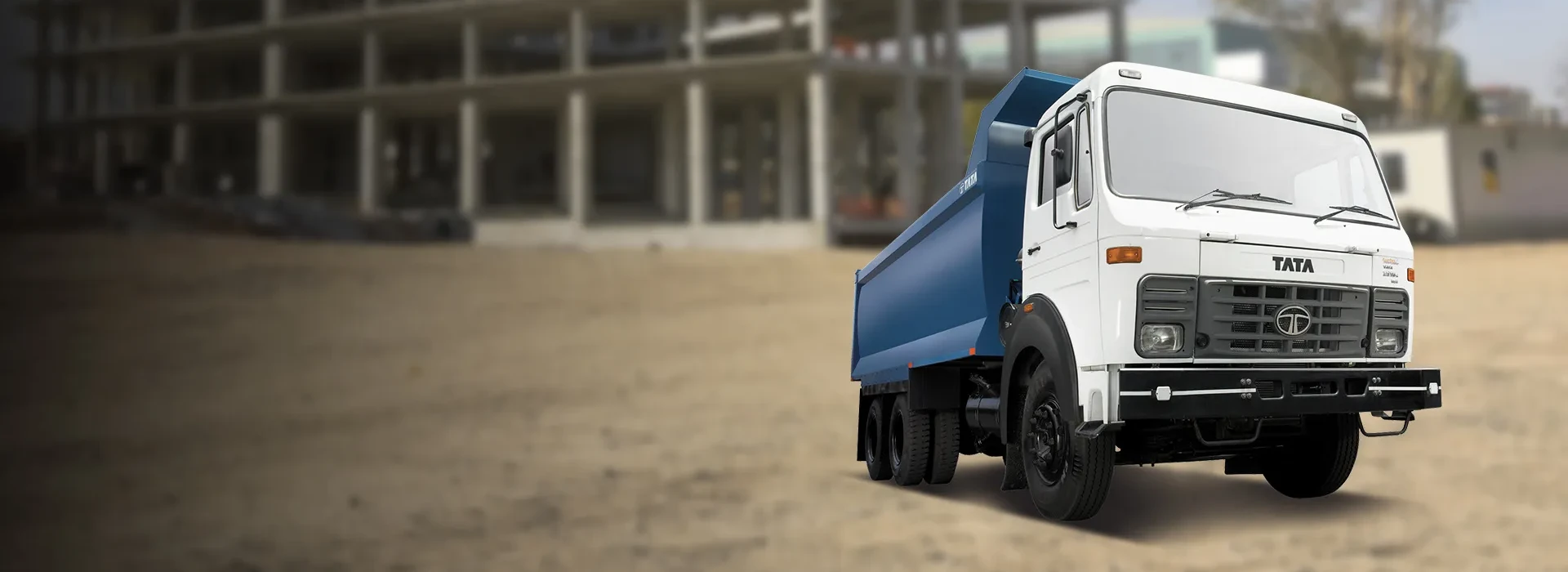White Tata LPK 2518 heavy-duty tipper truck with a blue dump bed parked in front of a building under construction