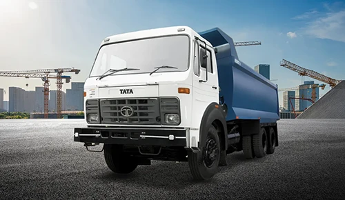 White Tata LPK 2518 heavy-duty tipper truck with a blue dump bed parked at a construction site with cranes and a city skyline in the background