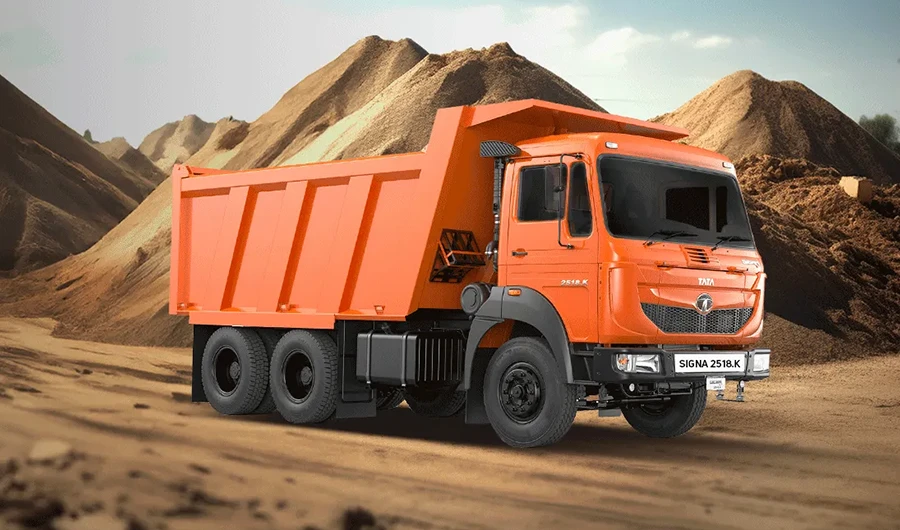 Orange Tata Signa 2518.K tipper truck parked in front of large earth mounds at a construction site.