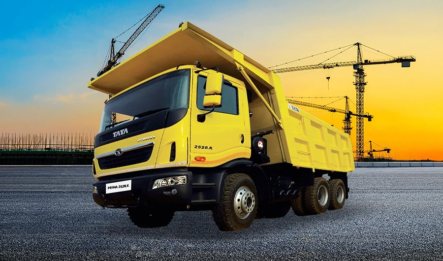 ellow Tata Prima 2528.K tipper truck with construction cranes and sunset sky