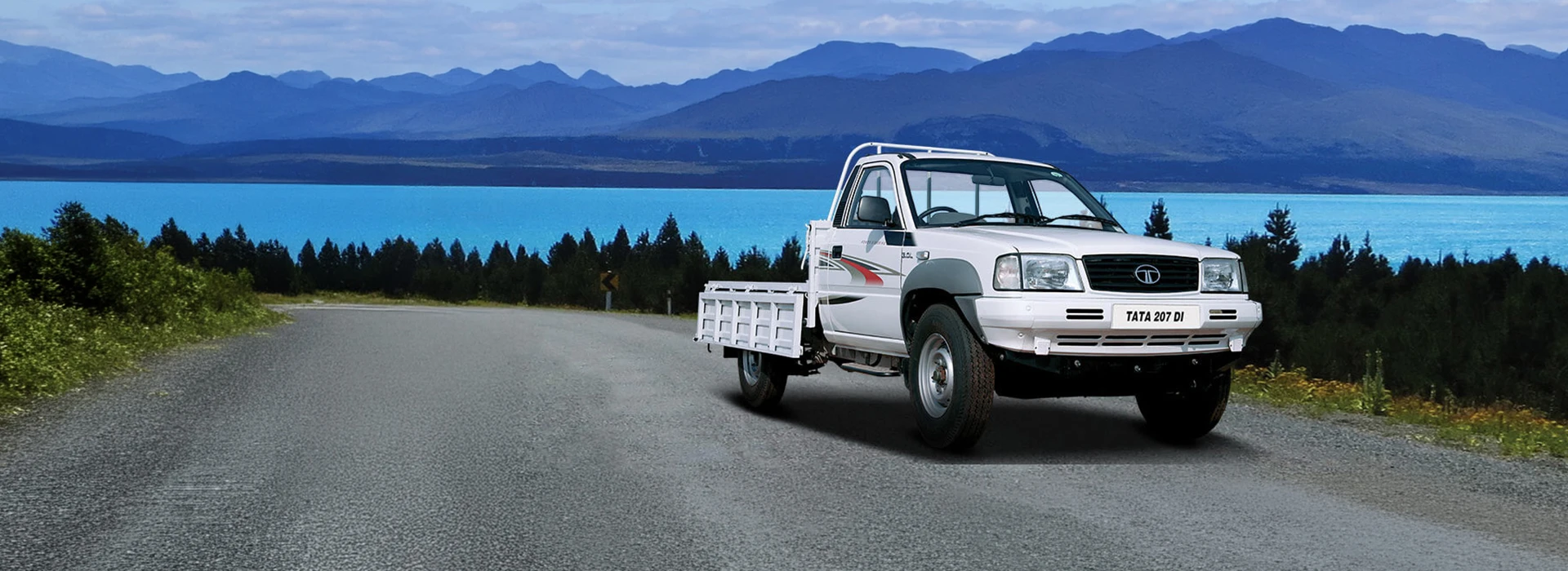 White Tata 207 DI single-cab pickup truck with a drop-side cargo bed parked on a scenic mountain road
