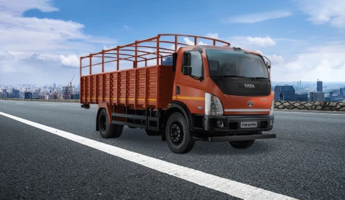 Orange Tata T.12 Ultra commercial truck with a high-sided open-cage load body parked on a road with city buildings in the background