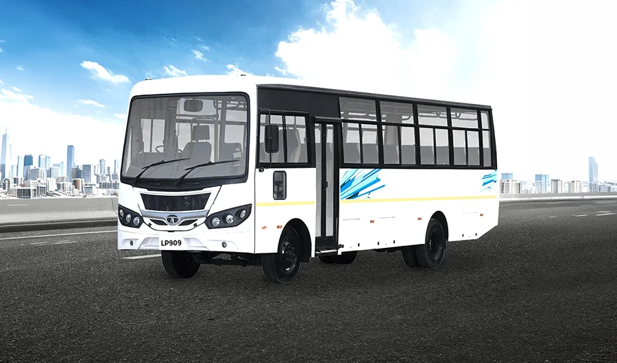 White Tata LP 909 passenger bus parked on an open road with a city skyline under a clear blue sky