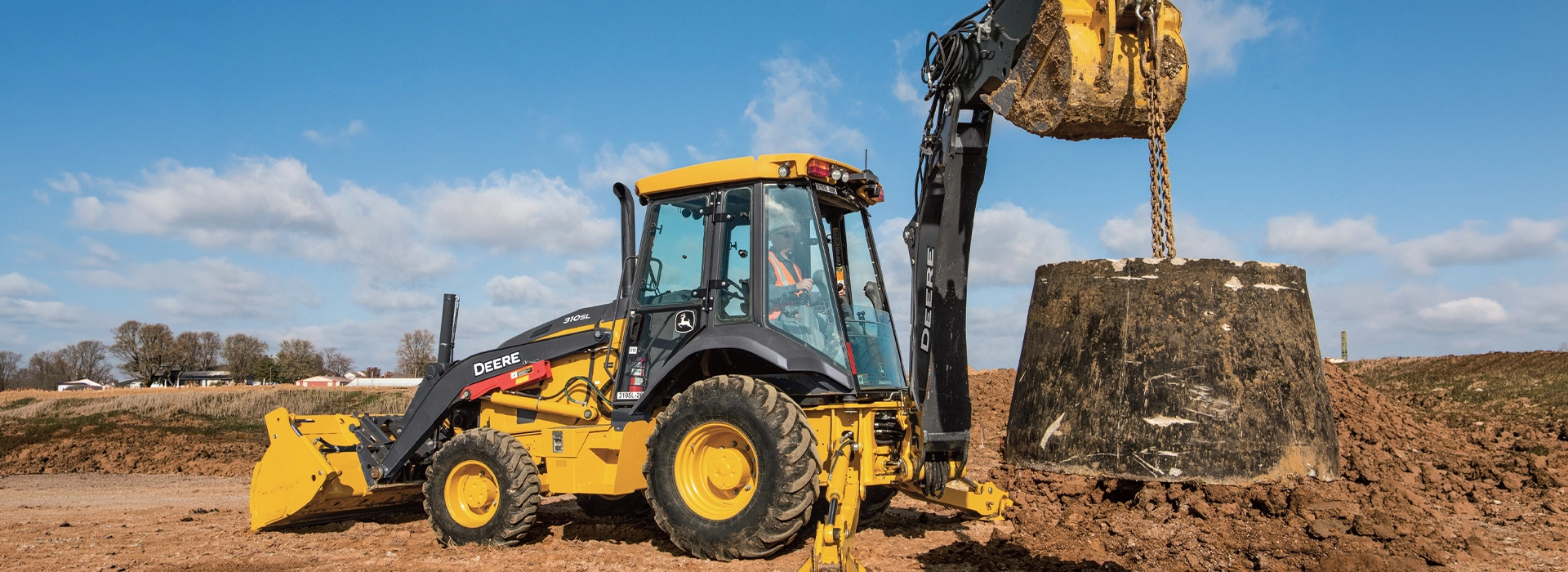 John Deere backhoe loader lifting a heavy concrete block at a construction site