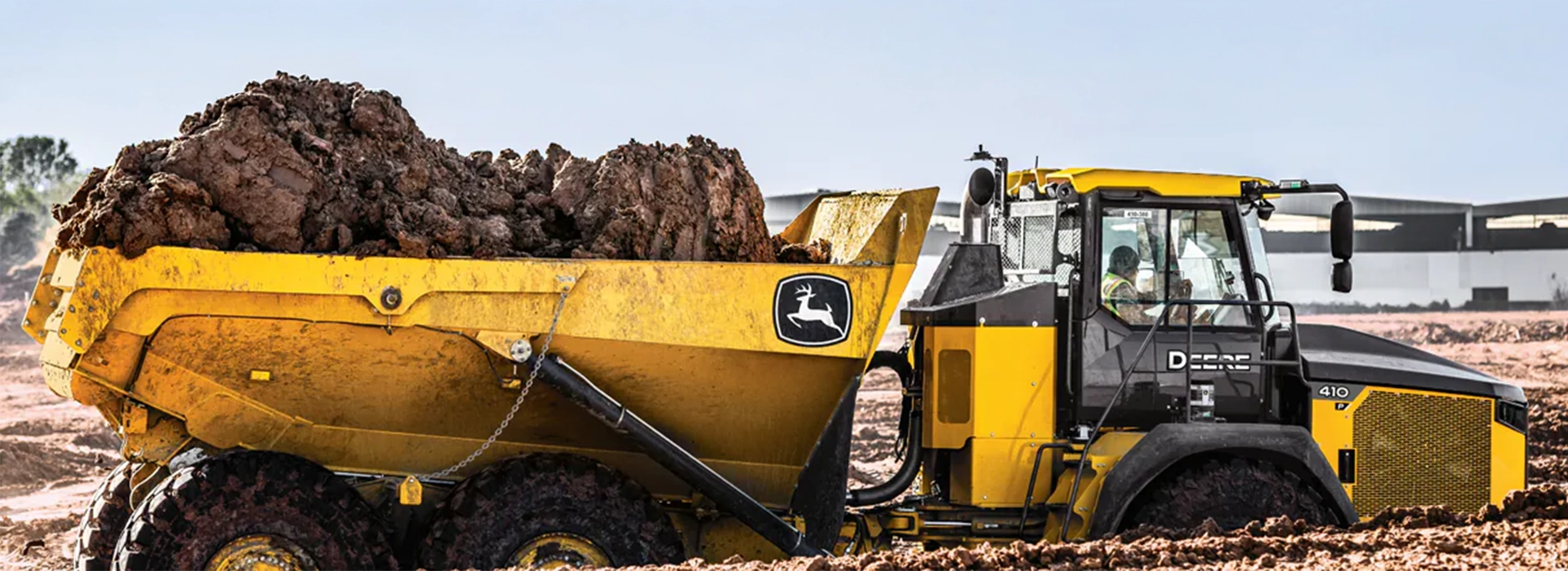 John Deere articulated dump truck transporting a heavy load of earth across a muddy construction site