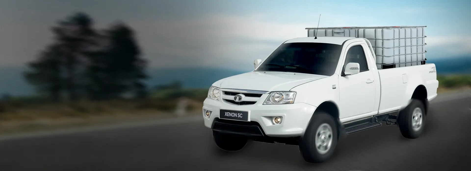 Front three-quarter view of a white Tata Xenon SC single cab bakkie loaded with a large liquid container driving on an asphalt road