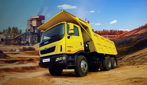Yellow Tata Prima 2528.K heavy-duty tipper truck in front of an industrial mining plant