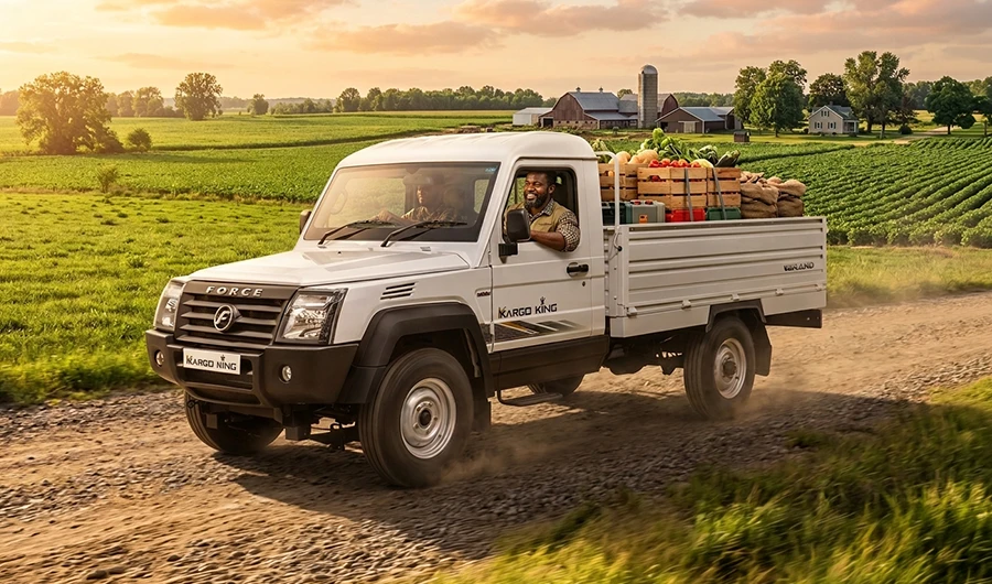 A white Force Kargo King pickup truck, loaded with fresh produce in wooden crates and burlap sacks, driving on a dirt road in a rural farm landscape during golden hour.