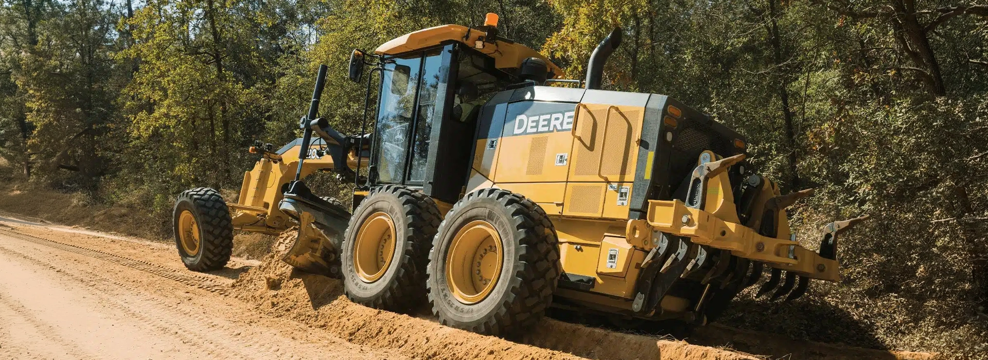 John Deere motor grader grading and levelling a dirt road at a construction site