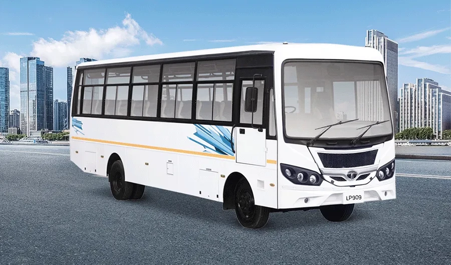 White Tata LP 909 passenger bus parked on an open road with a city skyline under a clear blue sky