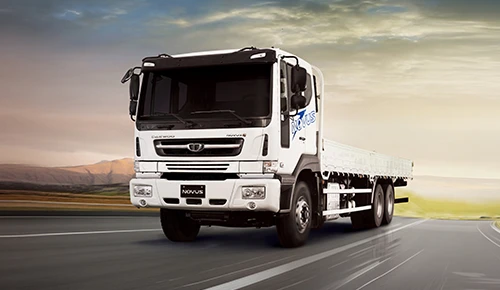 White Daewoo Novus flatbed truck driving along an open highway at sunset