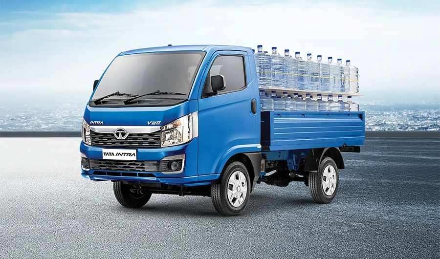 Blue Tata Intra V20 pickup truck loaded with large water bottles on a paved surface.
