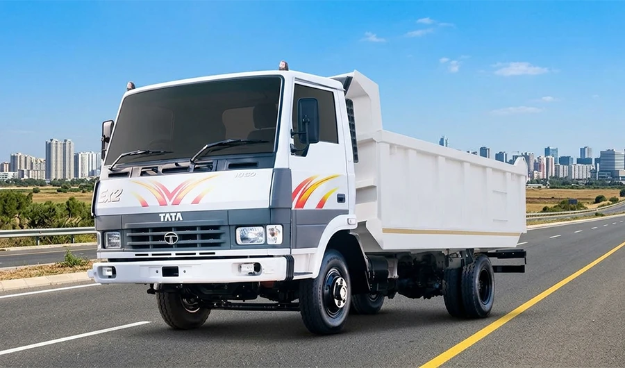A front three-quarter view of a white Tata LPK 813 Tipper truck driving on a asphalt highway, set against a background of a modern city skyline under a bright blue sky.